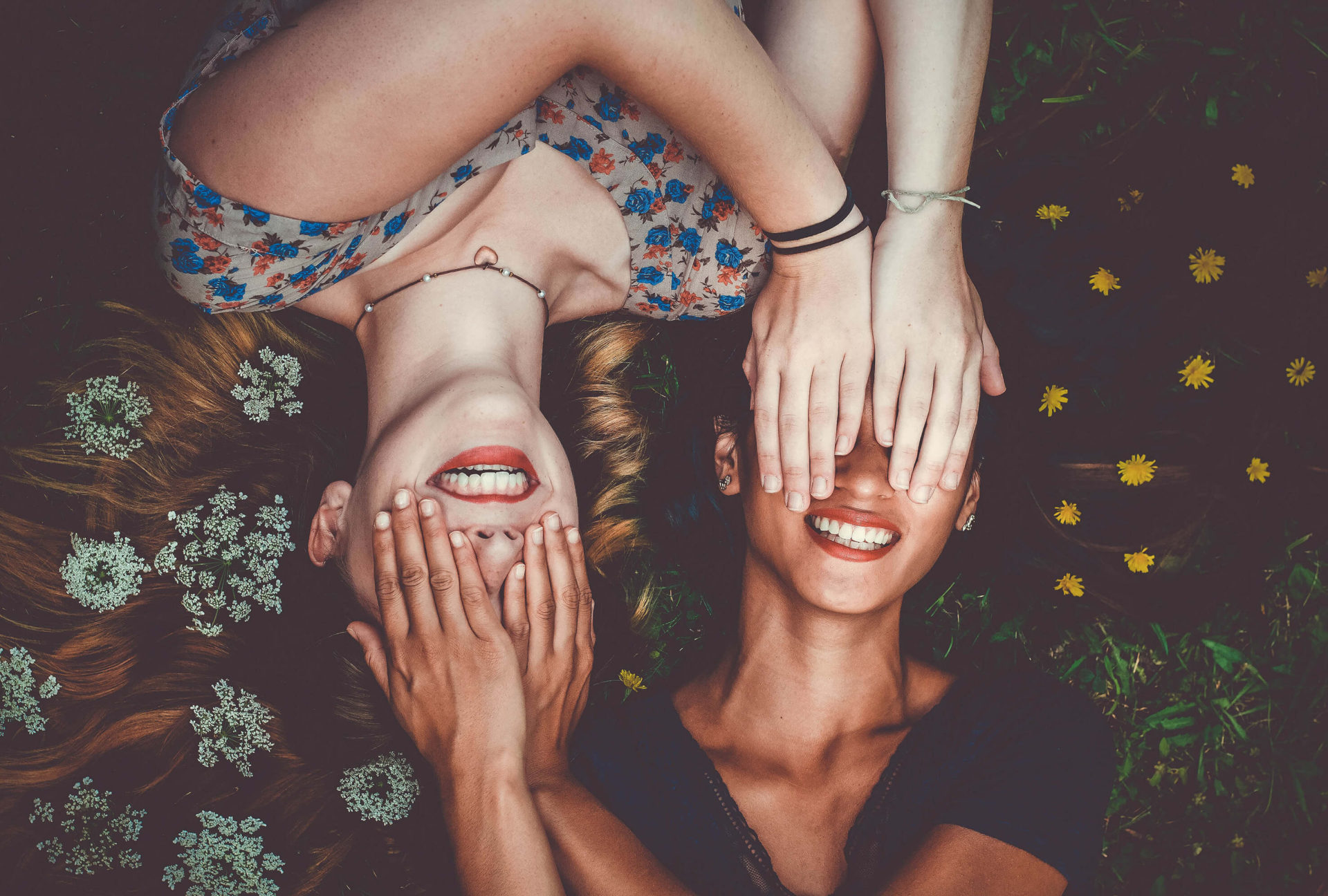 Dos chicas sonrientes tapándose los ojos mutuamente
